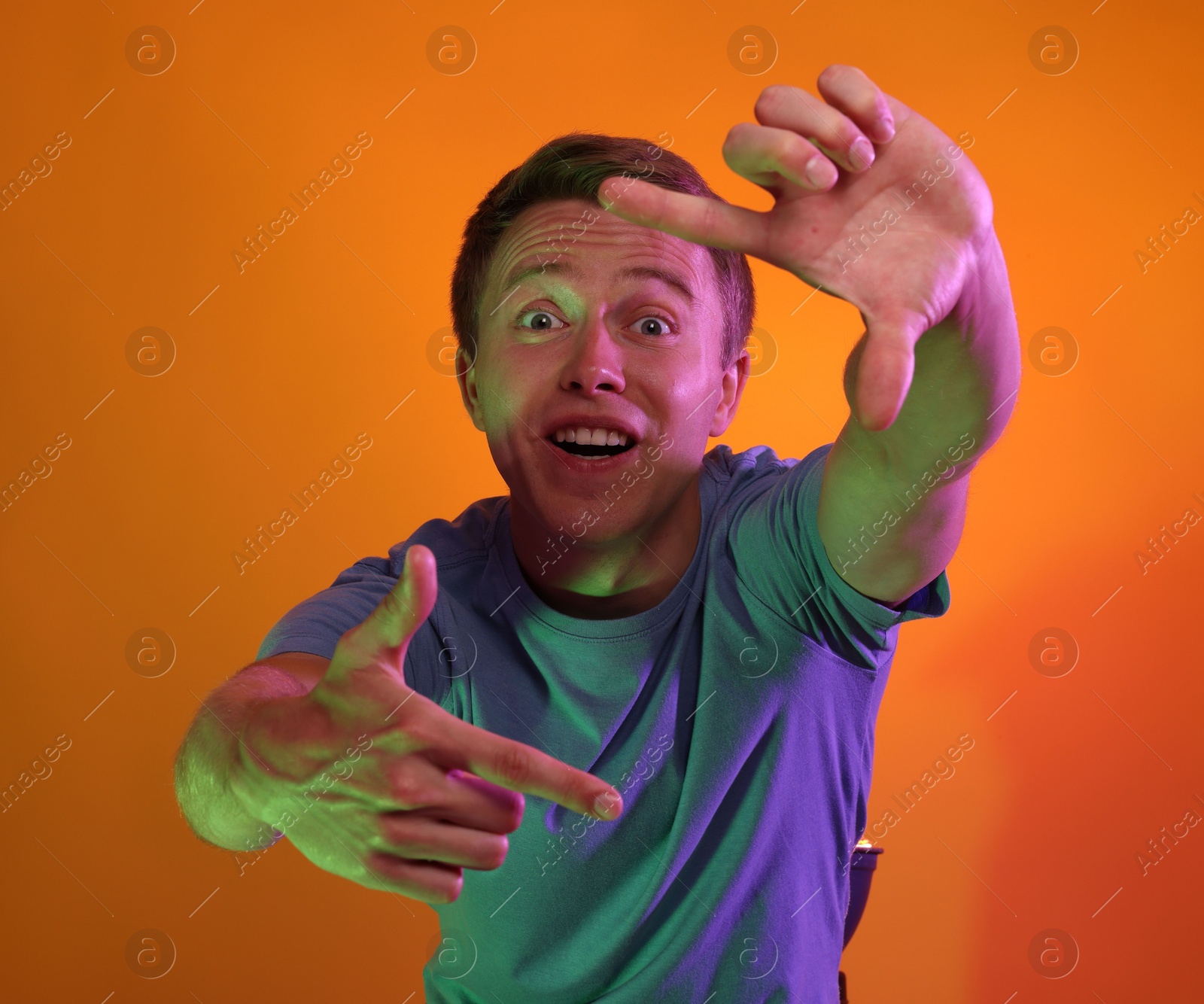 Emotional man showing frame gesture in neon lights against orange background Photo of Emotional man showing frame gesture in neon lights against orange background