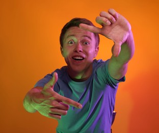 Photo of Emotional man showing frame gesture in neon lights against orange background