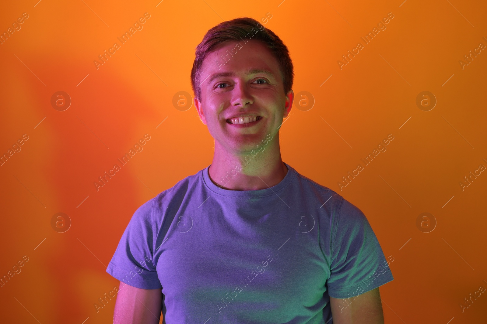 Photo of Portrait of smiling man in neon lights against orange background