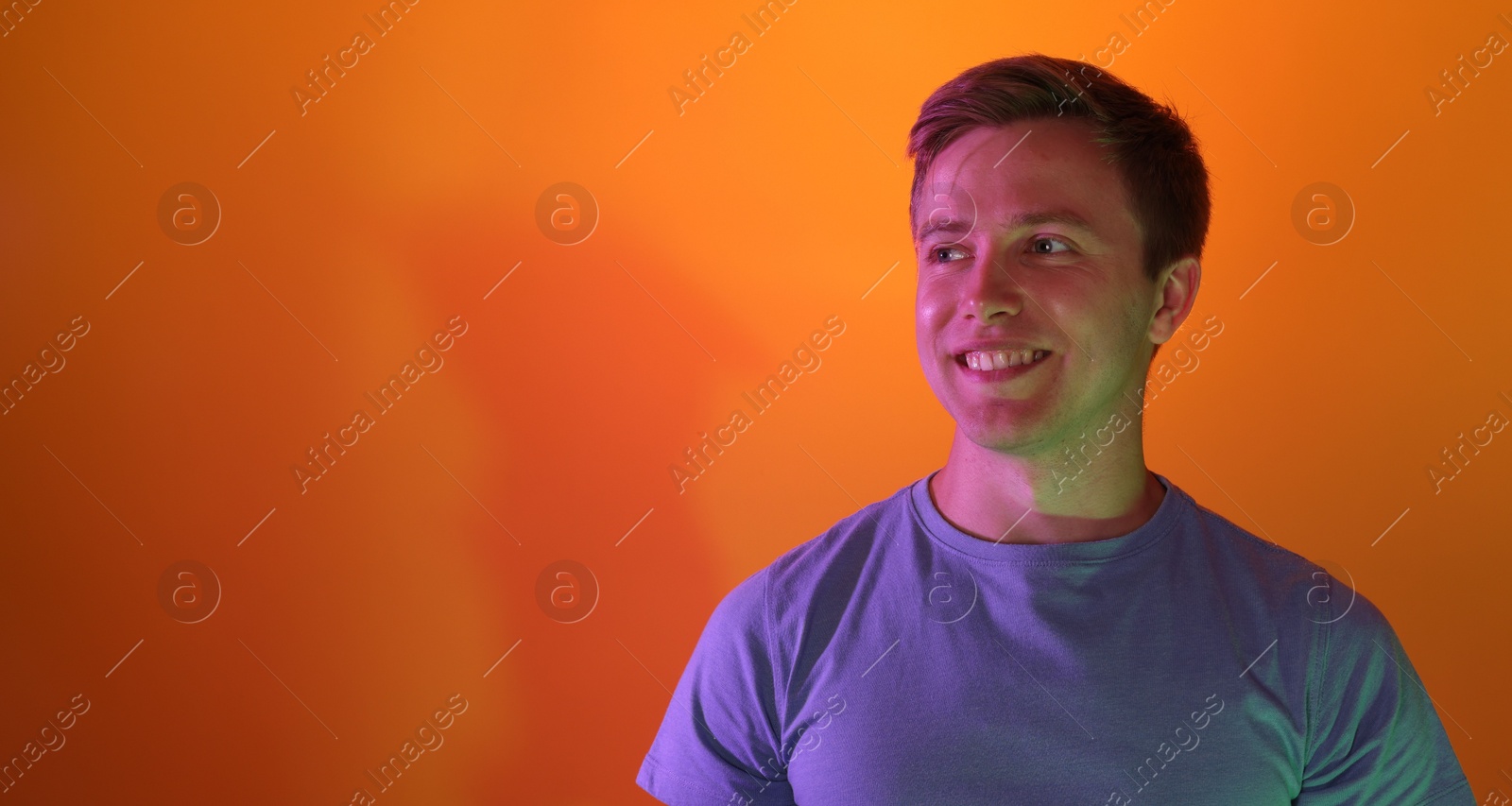 Photo of Smiling man in neon lights against orange background. Space for text
