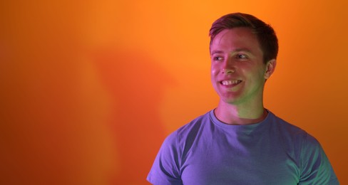 Photo of Smiling man in neon lights against orange background. Space for text