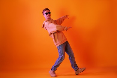 Photo of Smiling man wearing sunglasses dancing in neon lights against orange background