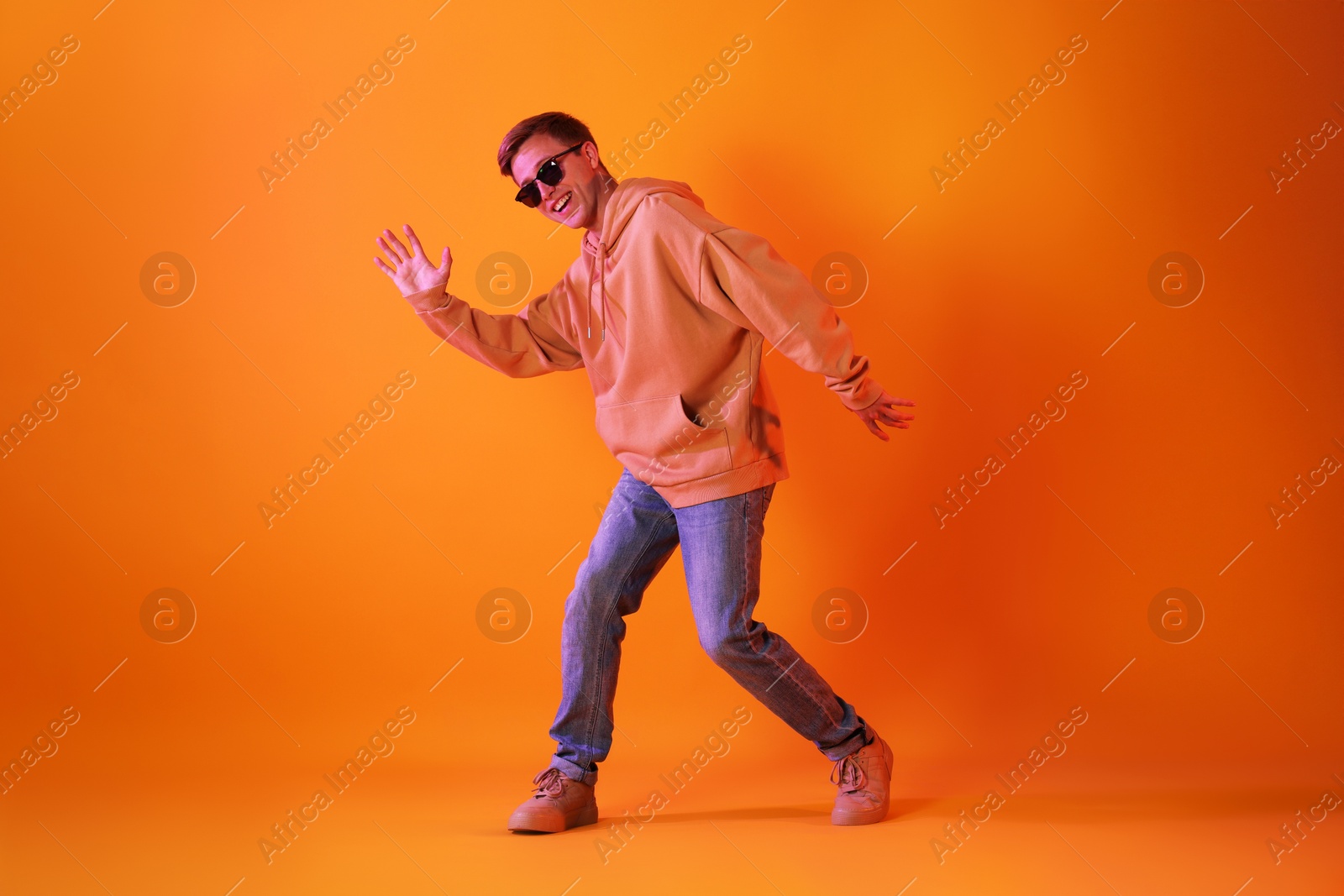 Smiling man wearing sunglasses dancing in neon lights against orange background Photo of Smiling man wearing sunglasses dancing in neon lights against orange background