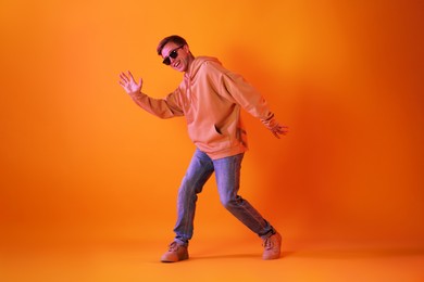Photo of Smiling man wearing sunglasses dancing in neon lights against orange background