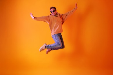 Photo of Happy man wearing sunglasses jumping in neon lights against orange background