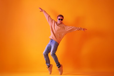 Photo of Smiling man wearing sunglasses dancing in neon lights against orange background