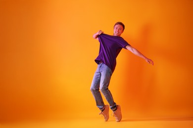 Photo of Smiling man dancing in neon lights against orange background. Space for text