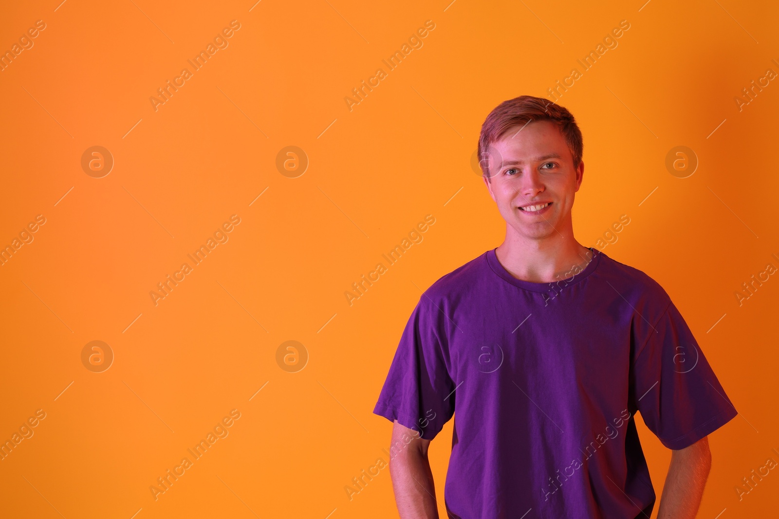 Portrait of smiling man in neon lights against orange background. Space for text Photo of Portrait of smiling man in neon lights against orange background. Space for text