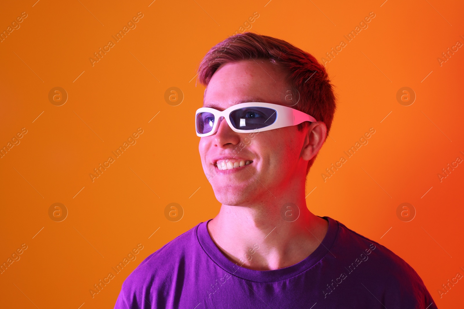 Smiling man wearing sunglasses in neon lights against orange background Photo of Smiling man wearing sunglasses in neon lights against orange background