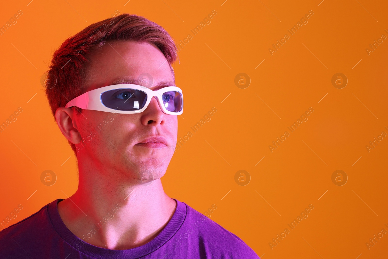 Handsome man wearing sunglasses in neon lights against orange background. Space for text Photo of Handsome man wearing sunglasses in neon lights against orange background. Space for text