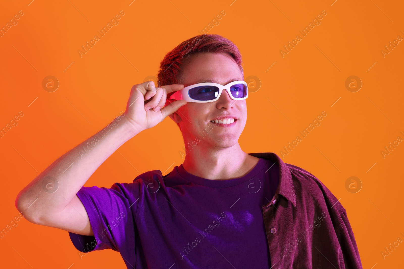 Smiling man wearing sunglasses in neon lights against orange background Photo of Smiling man wearing sunglasses in neon lights against orange background