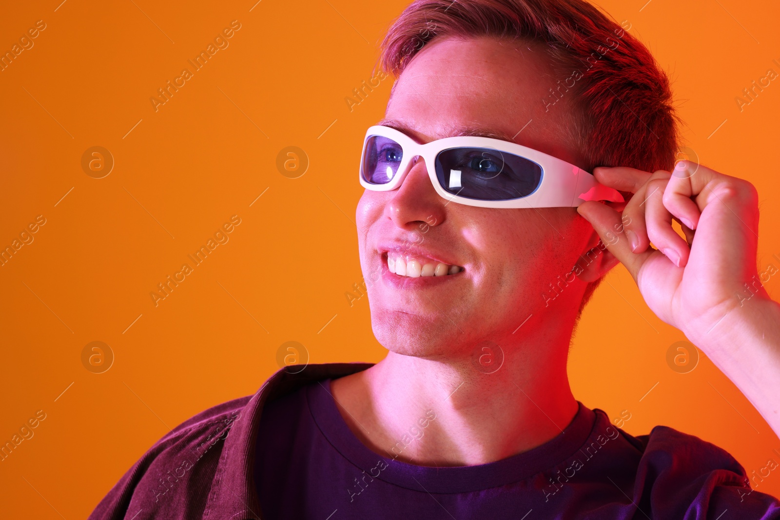 Smiling man wearing sunglasses in neon lights against orange background Photo of Smiling man wearing sunglasses in neon lights against orange background