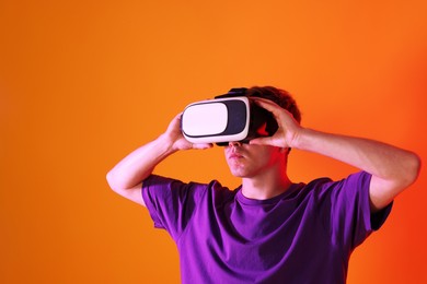 Photo of Man using virtual reality headset in neon lights against orange background. Space for text