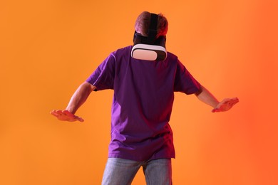 Photo of Man using virtual reality headset in neon lights against orange background