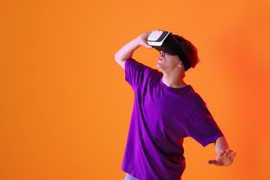 Photo of Man using virtual reality headset in neon lights against orange background. Space for text