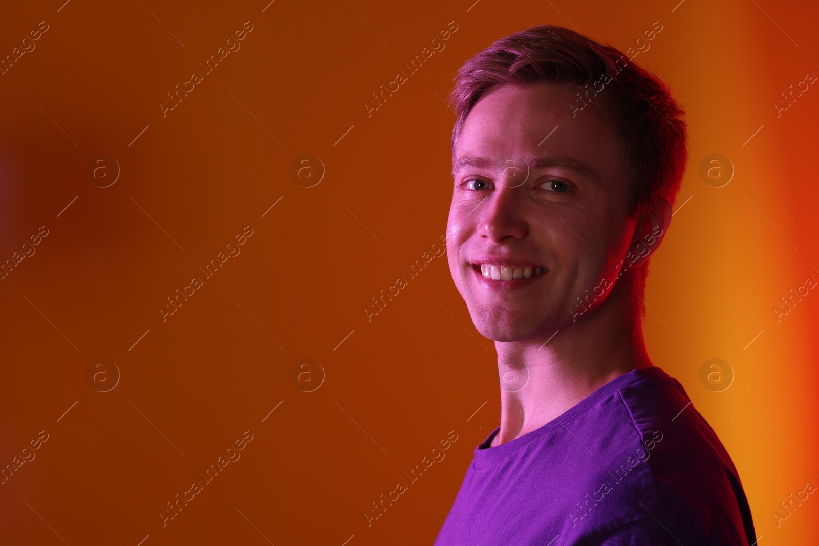 Portrait of smiling man in neon lights against orange background. Space for text Photo of Portrait of smiling man in neon lights against orange background. Space for text