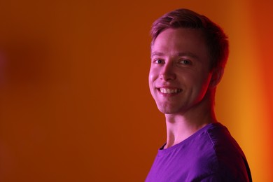 Photo of Portrait of smiling man in neon lights against orange background. Space for text