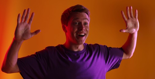 Photo of Emotional man raising hands in neon lights against orange background