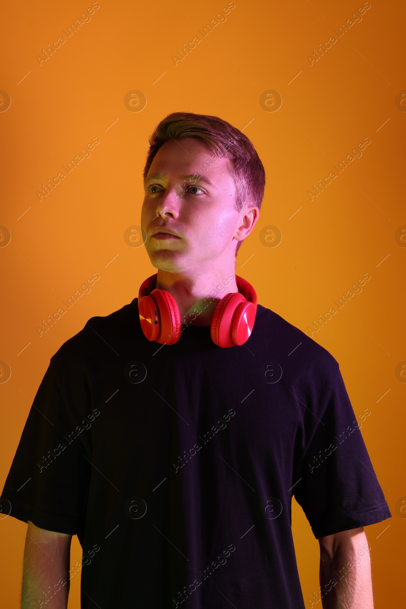 Handsome man with headphones in neon lights against orange background Photo of Handsome man with headphones in neon lights against orange background