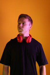Photo of Handsome man with headphones in neon lights against orange background