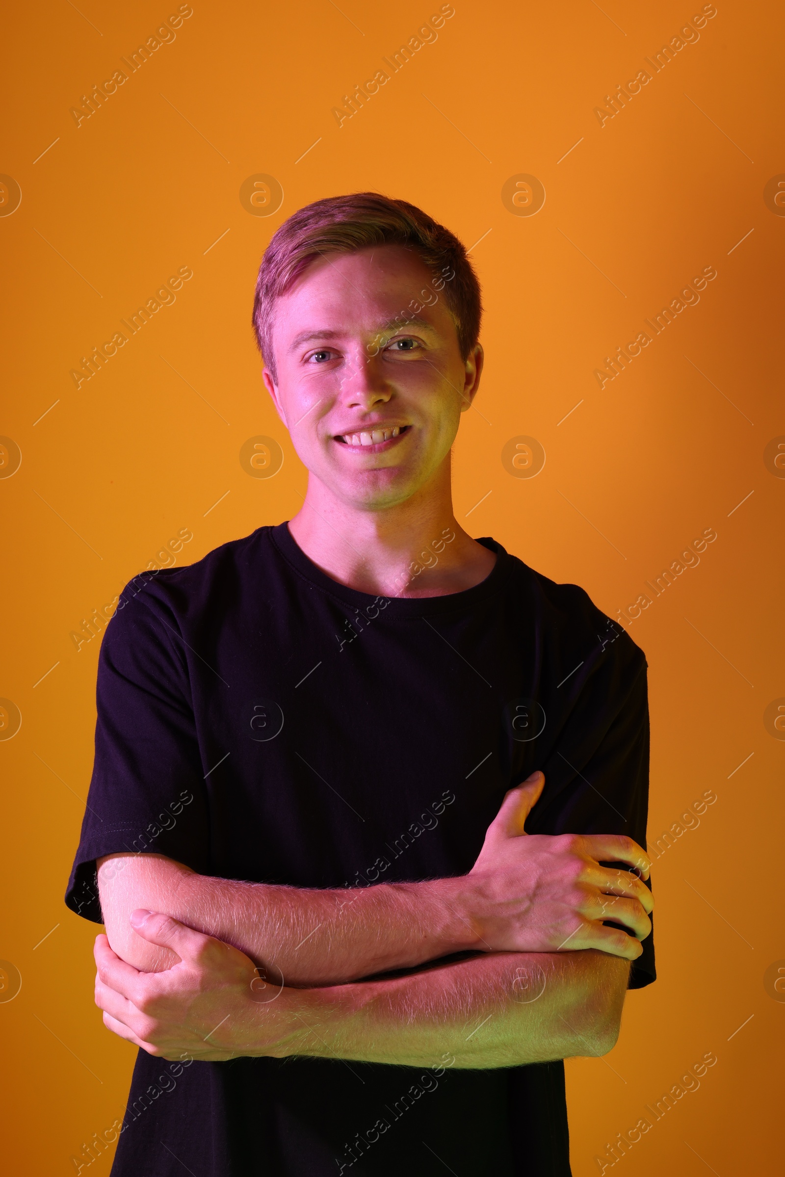 Portrait of smiling man in neon lights against orange background Photo of Portrait of smiling man in neon lights against orange background
