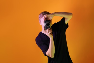 Photo of Man with camera taking photo in neon lights against orange background. Space for text