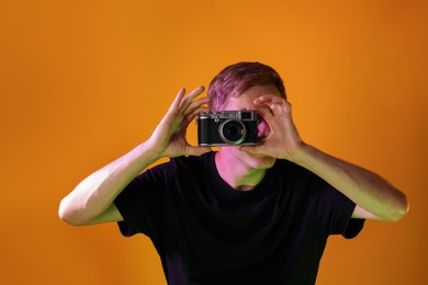 Photo of Man with camera taking photo in neon lights against orange background