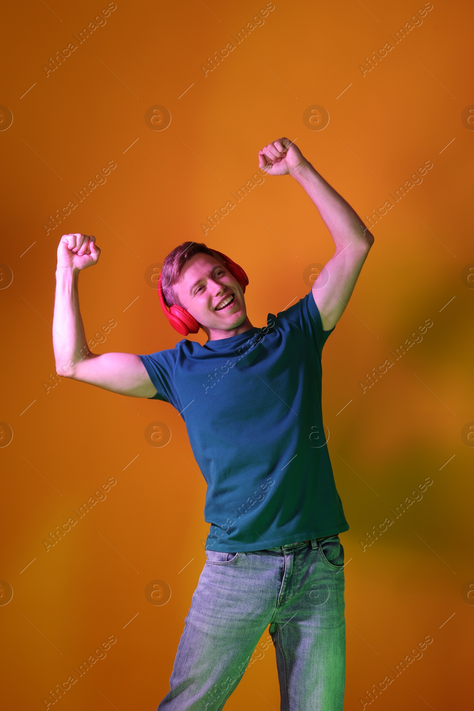 Smiling man wearing headphones listening to music in neon lights against orange background Photo of Smiling man wearing headphones listening to music in neon lights against orange background