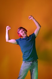 Photo of Smiling man wearing headphones listening to music in neon lights against orange background