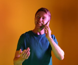 Photo of Happy man talking on smartphone in neon lights against orange background