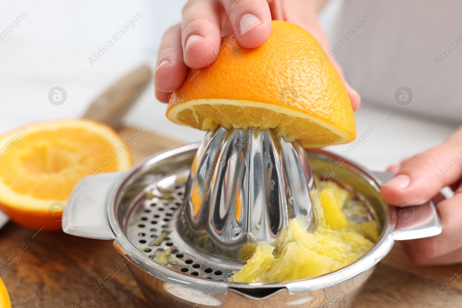 Making juice. Woman with orange using juicer at table indoors, closeup Photo of Making juice. Woman with orange using juicer at table indoors, closeup