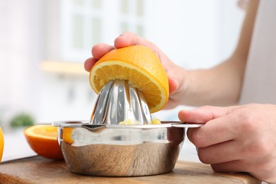 Photo of Making juice. Woman with orange using juicer at table indoors, closeup