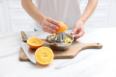 Photo of Making juice. Woman with orange using juicer at white marble table indoors, closeup