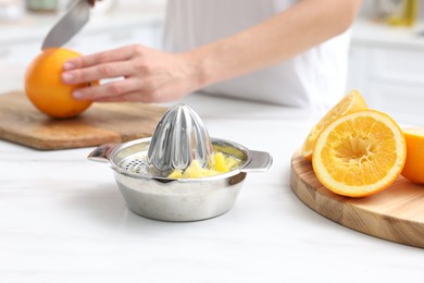 Photo of Making juice. Woman cutting orange at white marble table indoors, focus on juicer and fruits