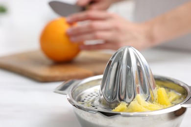 Photo of Making juice. Woman cutting orange at white marble table indoors, focus on juicer