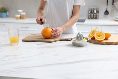 Photo of Making juice. Woman cutting orange at white marble table indoors, closeup