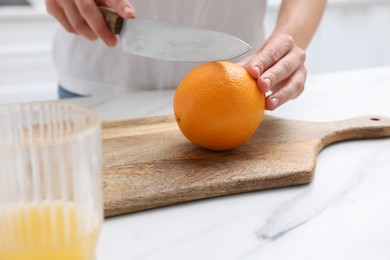Photo of Making juice. Woman cutting orange at white marble table indoors, closeup