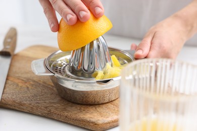 Photo of Making juice. Woman with orange using juicer at white table indoors, closeup