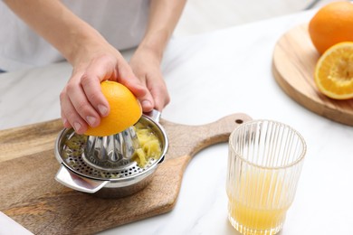 Photo of Making juice. Woman with orange using juicer at white marble table indoors, closeup