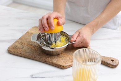 Photo of Making juice. Woman with orange using juicer at white marble table indoors, closeup