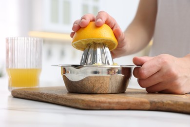Photo of Making juice. Woman with orange using juicer at white marble table indoors, closeup