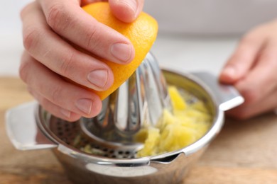 Photo of Making juice. Woman with orange using juicer at table indoors, closeup