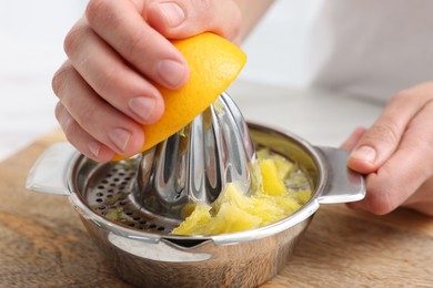 Photo of Making juice. Woman with orange using juicer at table indoors, closeup