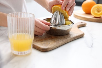 Photo of Making juice. Woman with orange using juicer at white marble table indoors, closeup