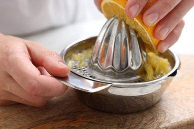 Photo of Making juice. Woman with orange using juicer at table indoors, closeup