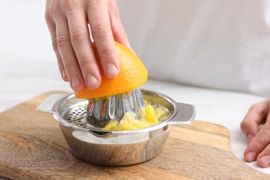 Photo of Making juice. Woman with orange using juicer at table indoors, closeup