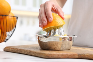 Photo of Making juice. Woman with orange using juicer at white marble table indoors, closeup