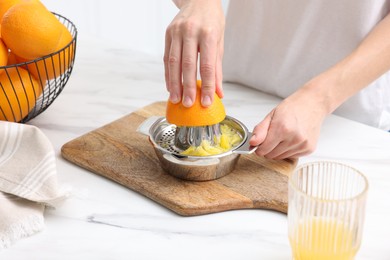 Photo of Making juice. Woman with orange using juicer at white marble table indoors, closeup