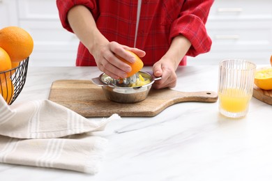 Photo of Making juice. Woman with orange using juicer at white marble table indoors, closeup