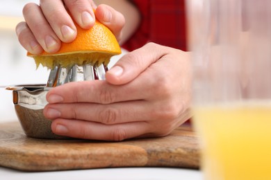 Photo of Making juice. Woman with orange using juicer at table indoors, closeup